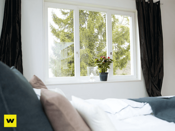 Helles Schlafzimmer mit großem Fenster, Blick ins Grüne und einer Pflanze auf der Fensterbank.