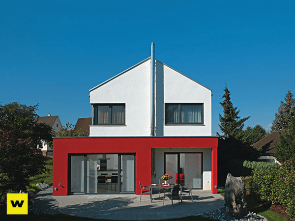 Modernes Einfamilienhaus mit roter Fassade und Terrasse im grünen Garten bei Sonnenschein.