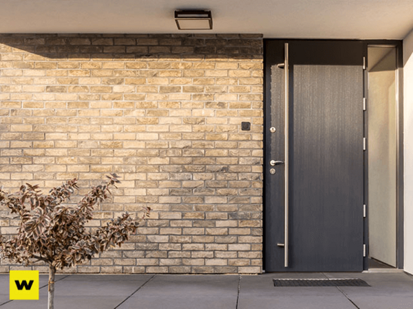 Moderne Haustür aus dunklem Material in einer Fassade mit hellen Klinkersteinen.